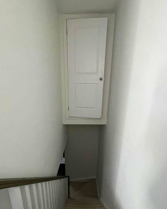 Small white door at the top of a staircase in a narrow hallway.