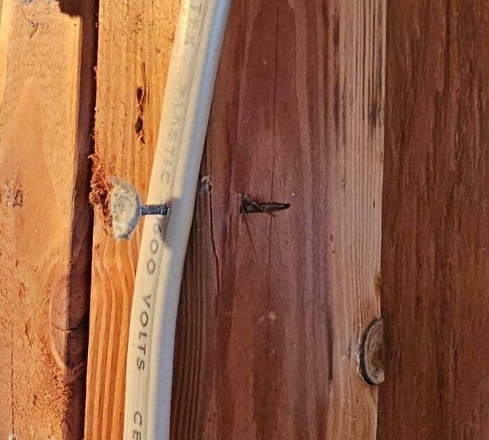 Electrical wiring through damaged wood wall with visible cracks and poor installation.