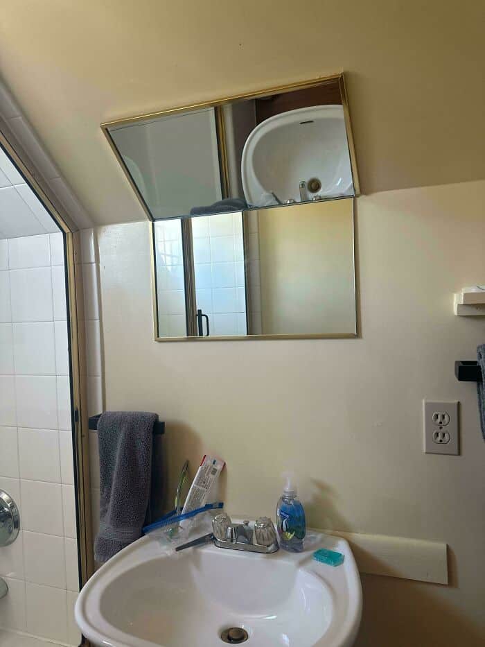 Unaligned bathroom mirror with a sink and towel rack below, reflecting a small bathroom with a showe.