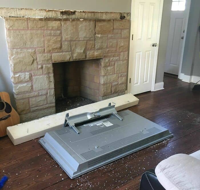 Fireplace with damaged mantel and fallen TV mount on hardwood floor.