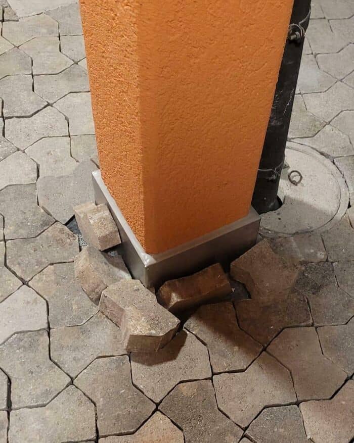 Damaged building corner with loose bricks and cracked pavement.