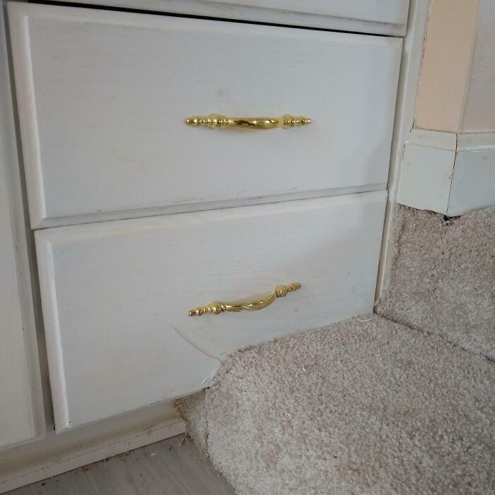 Broken dresser drawer with chipped wood and frayed carpet edge.