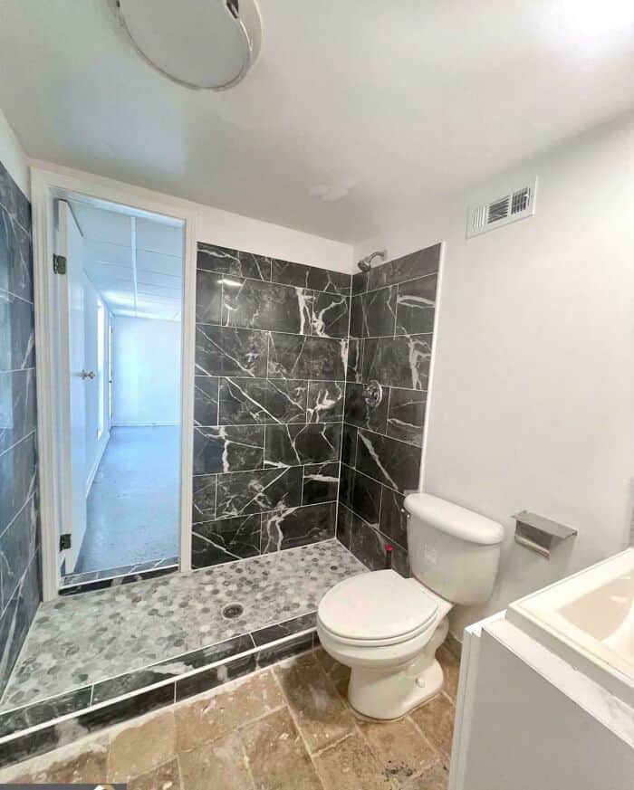 Unprofessional bathroom remodel featuring mismatched tiles and an awkward shower setup.