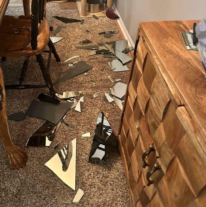 Broken mirror shards scattered across the carpet after accidental fall.