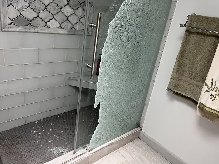 Broken glass shower door with shattered glass panel in a bathroom.