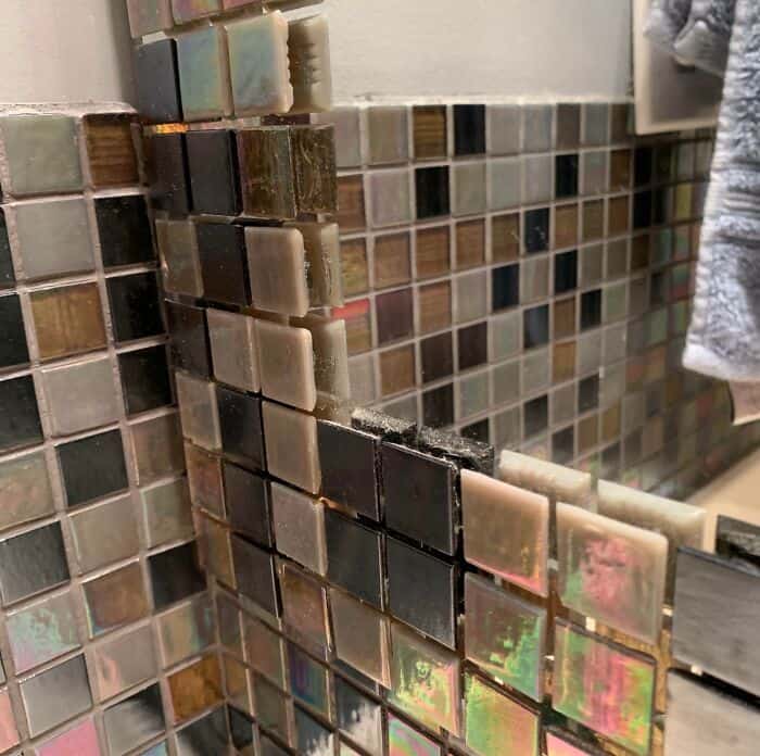 Misaligned mosaic tile wall with uneven grout lines and poor craftsmanship.