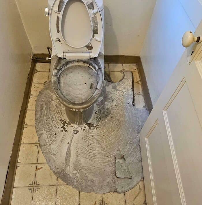 Toilet with uneven flooring and visible damage, illustrating a failed home improvement project.