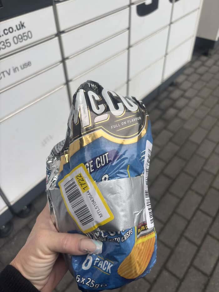 Hand holding a cheese snack pack with foil wrapper outdoors.