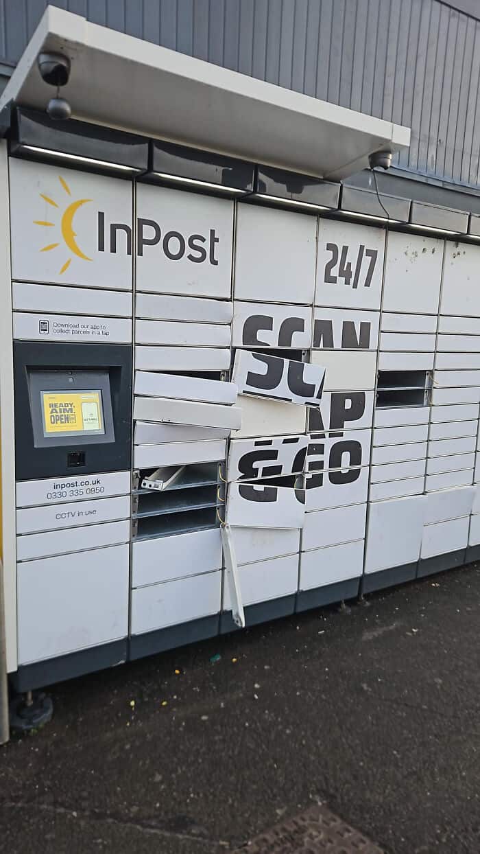 Damaged USPS mailbox with broken lock and displaced mail slots outside a building.