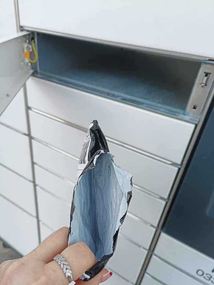 Mail collection box with an open slot, hand holding a torn metallic pouch ready for mailing.