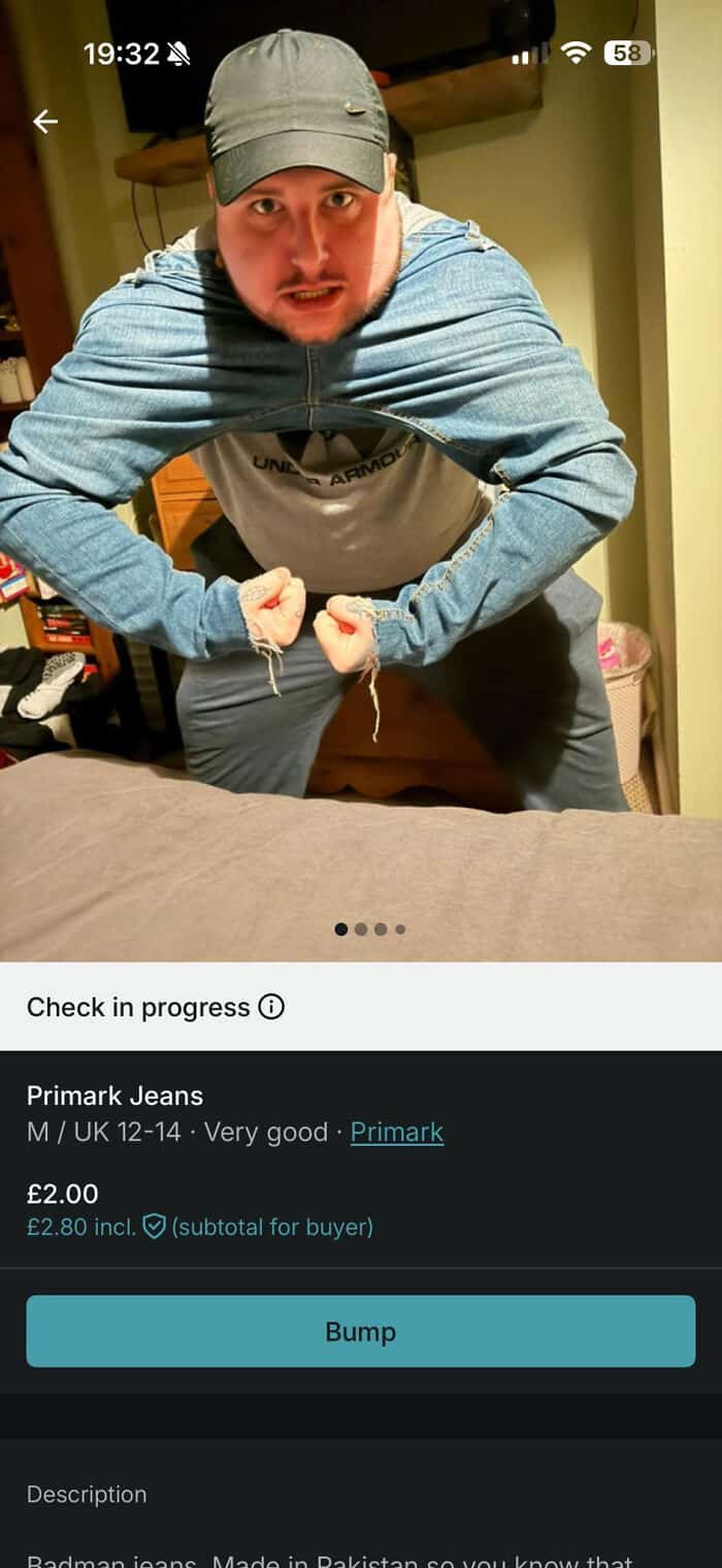 Man showing off muscles in pleated jeans, wearing a cap and hoodie indoors.