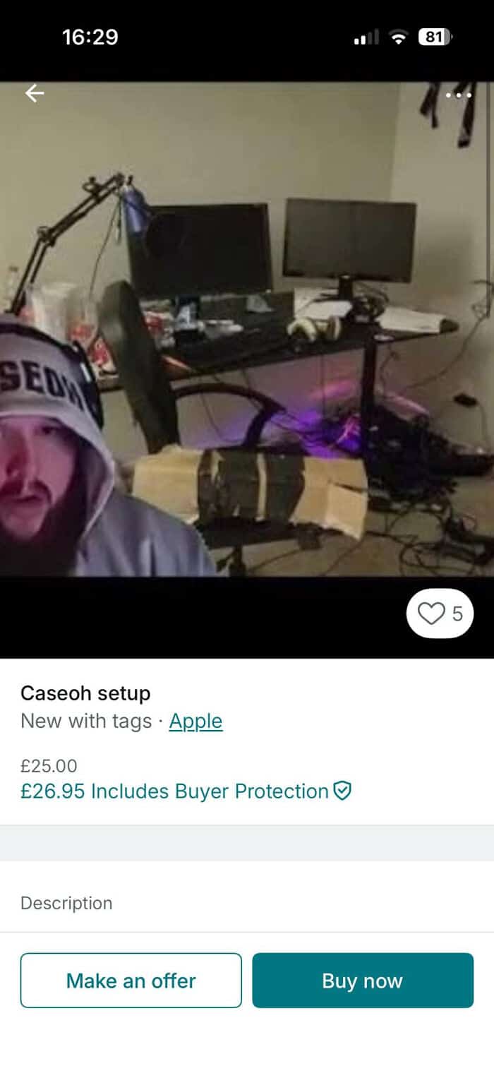 Setup with dual monitors, gaming gear, and a person in a hoodie in a cluttered room.
