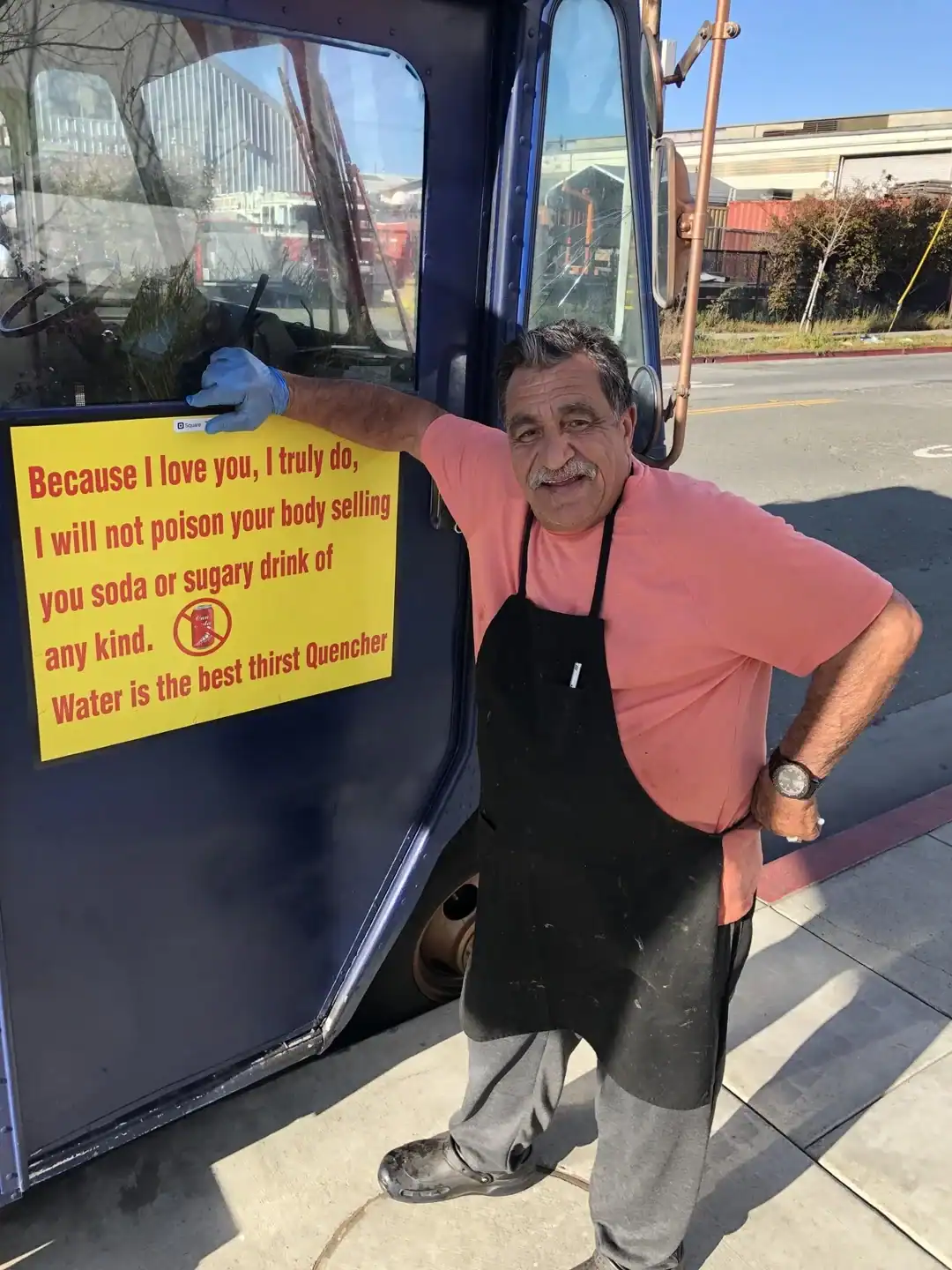 Man with humorous sign on food truck window.