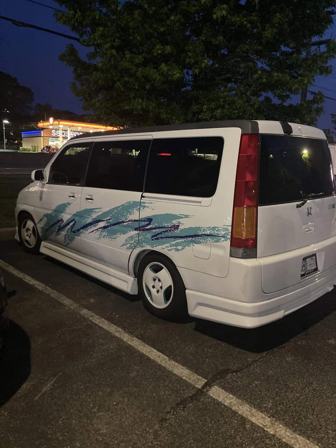 White mini van with blue wave graphic parked at night in a lot.