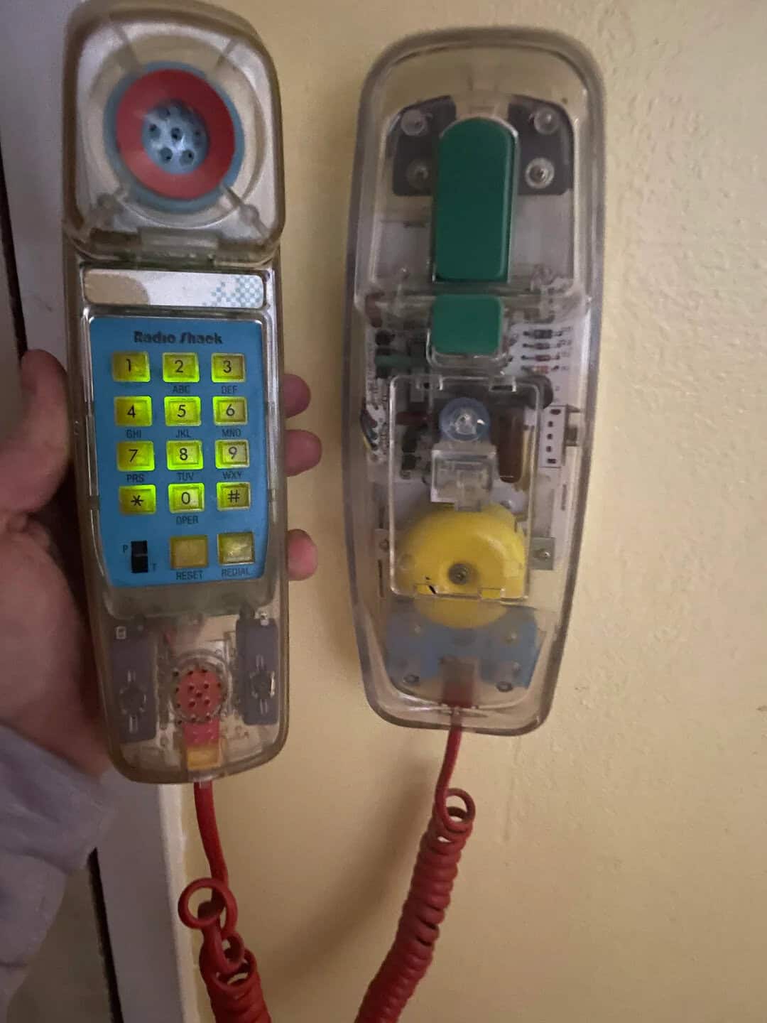 Vintage transparent payphone with colorful keypad and rotary dial, mounted on a yellow wall for publ.