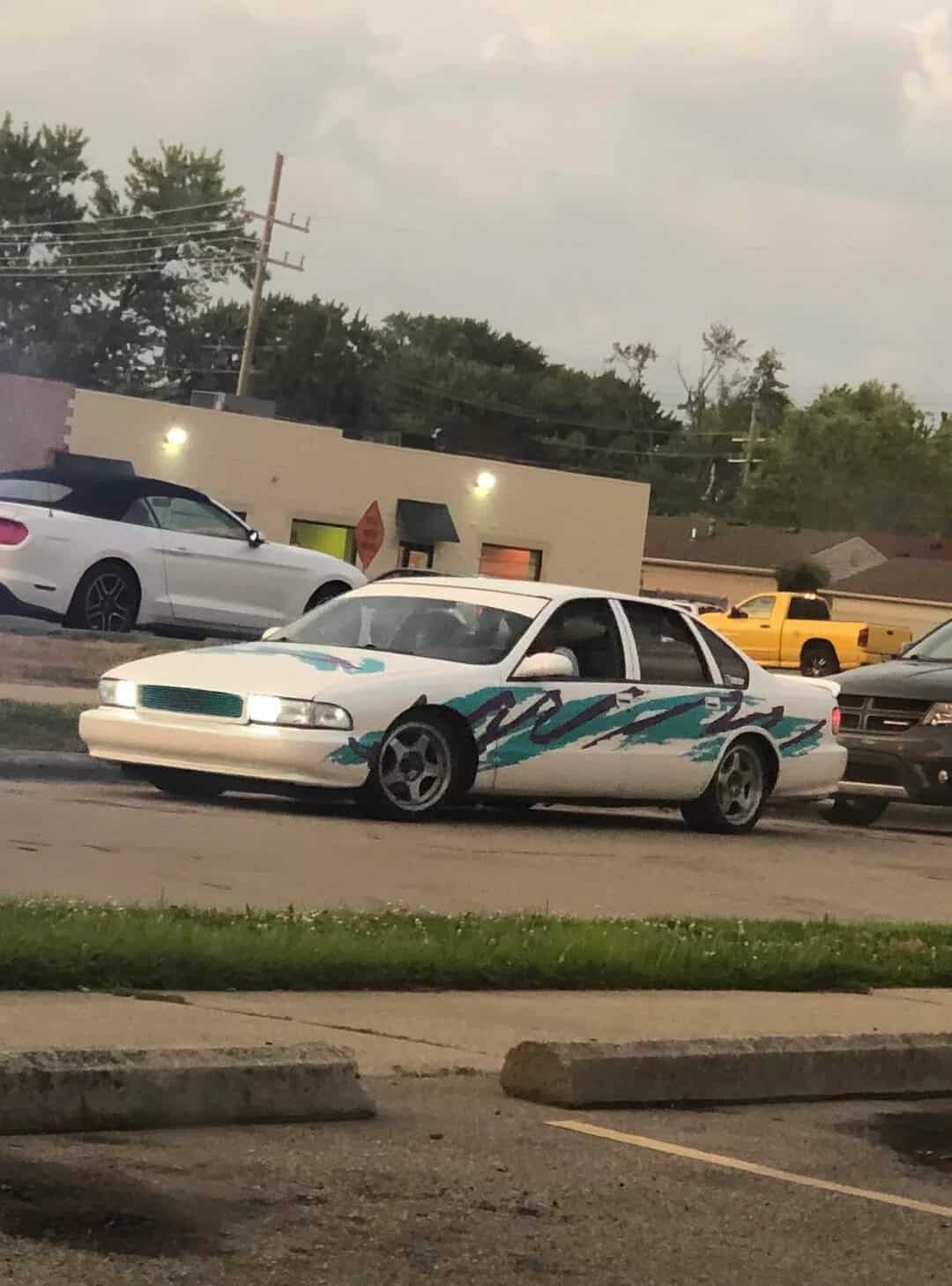 White car with blue and teal flame decals parked in a lot.