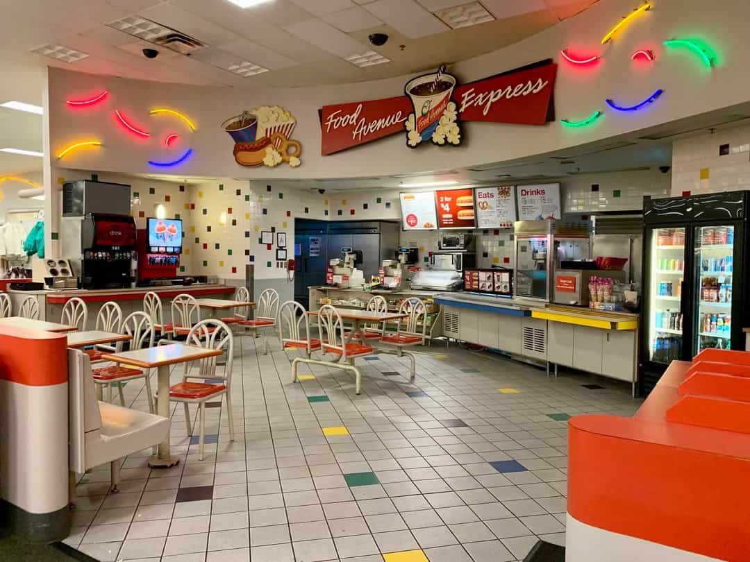 Bright food court with colorful neon lights, seating area, and snack counters.