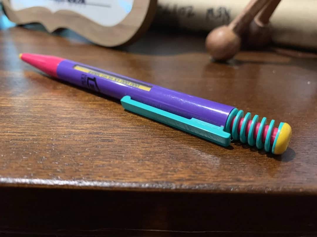 Pink and purple gel pen with teal clip on wooden desk, close-up shot.