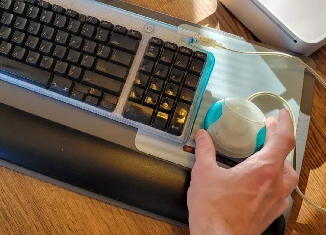 A close-up of a person's hand using a computer mouse next to a keyboard on a wooden desk.