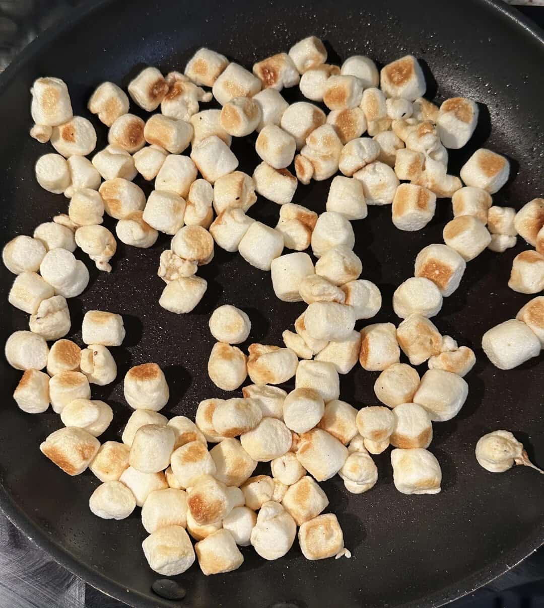 An image of small, toasted marshmallows in a black skillet, showcasing their golden-brown edges and.