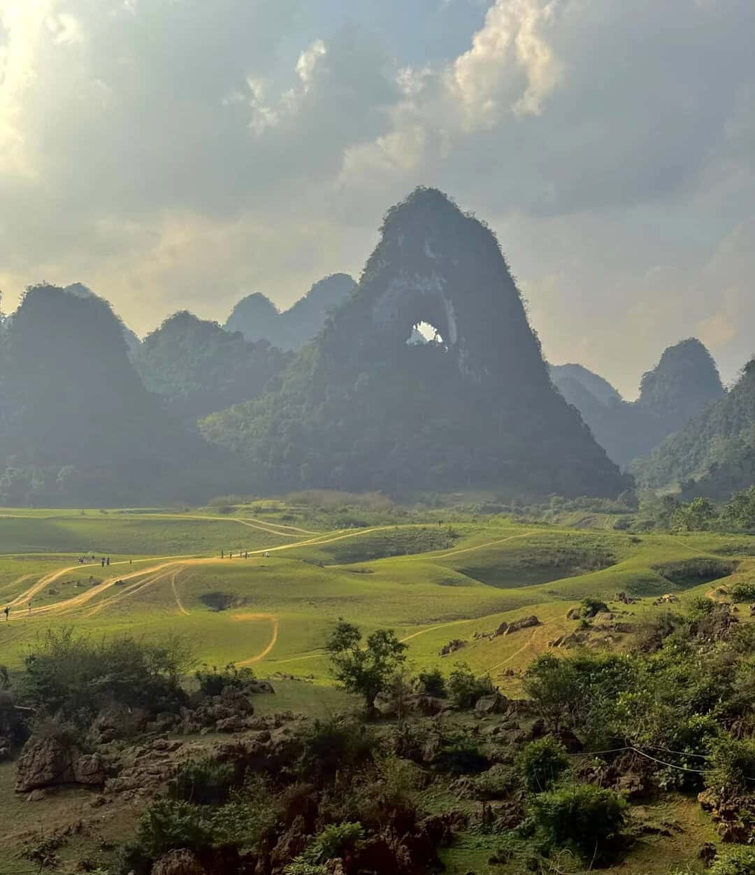 Scenic mountain landscape featuring lush green fields and a prominent arch-shaped mountain formation.