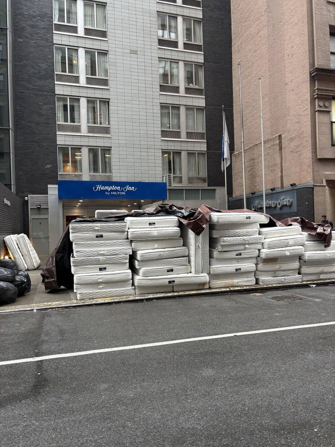 Stack of mattresses piled outside a city hotel, with surrounding buildings and street in the backgro.