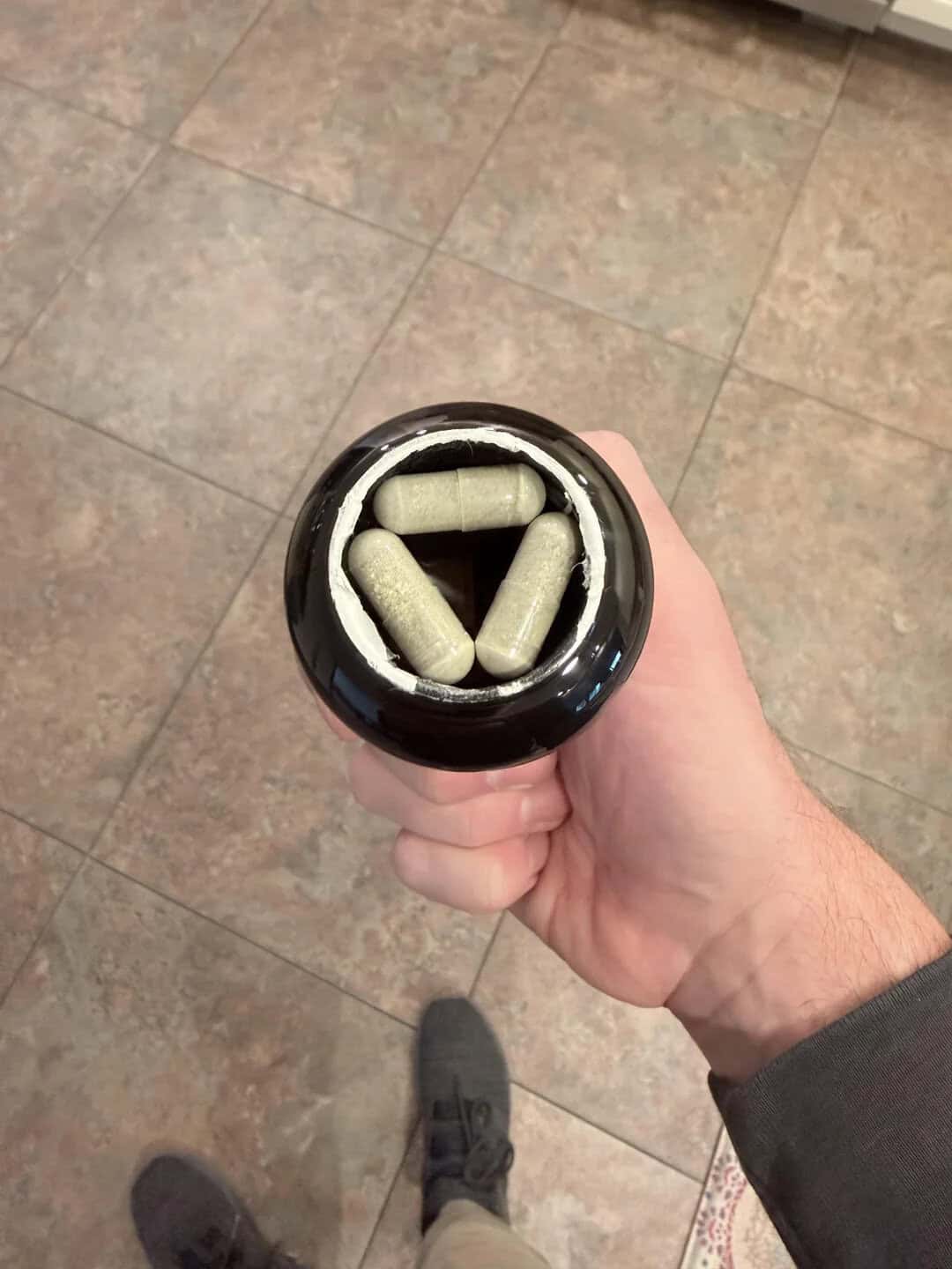 Hand holding a supplement bottle with capsules, viewed from above on tiled floor.