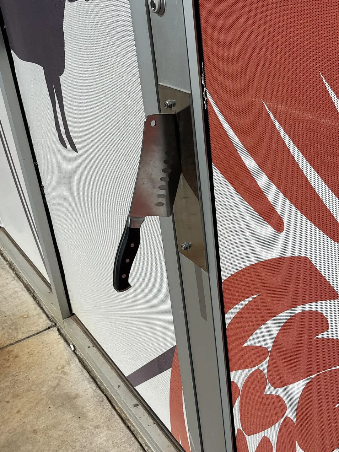 Unusual sight of a large kitchen knife embedded in a door handle. The knife appears to be securely l.