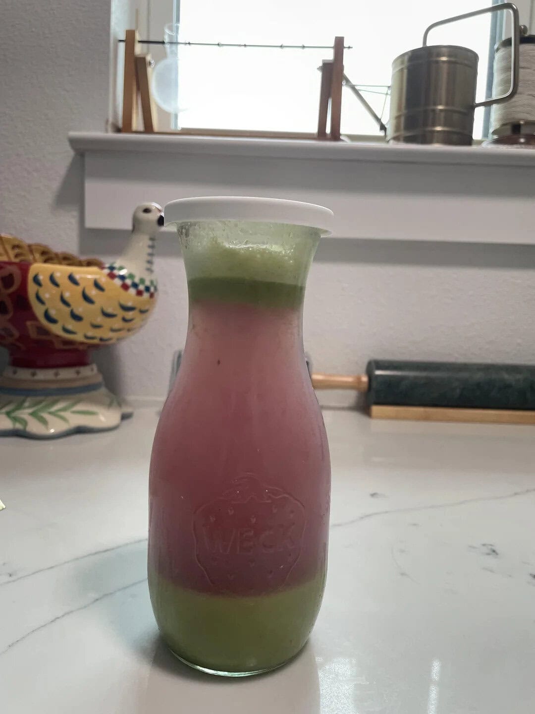 Bright, colorful smoothie with layered green and pink hues in a tall glass on a kitchen counter.