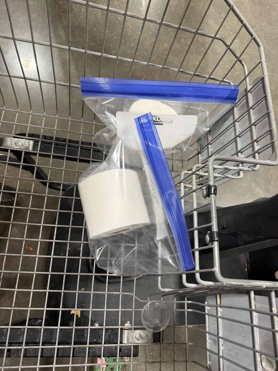 Shopping cart containing toilet paper and soap in a grocery store aisle.