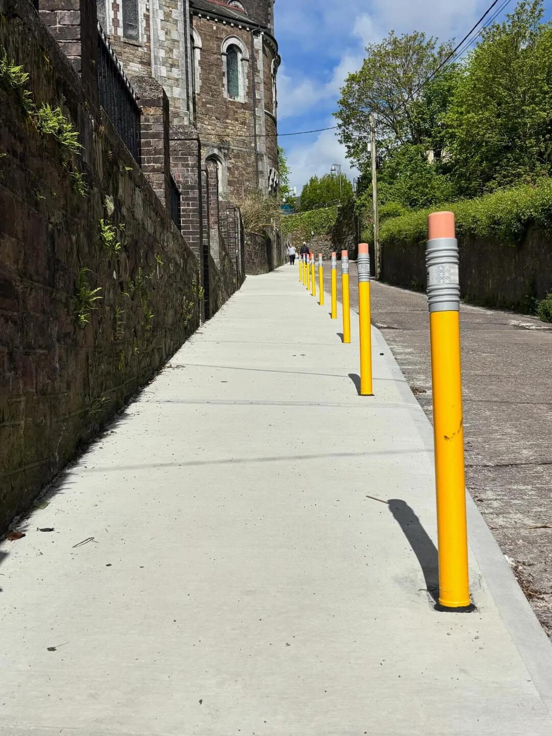 Empty sidewalk with yellow bollards and historic building in the background.