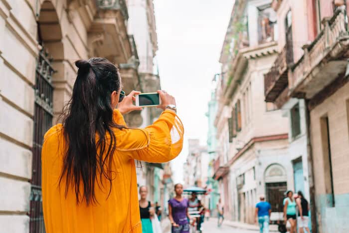 Woman in yellow jacket taking photo with smartphone on urban street.