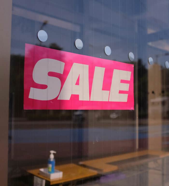 Bright pink sale sign on store window promoting discounts and special offers.