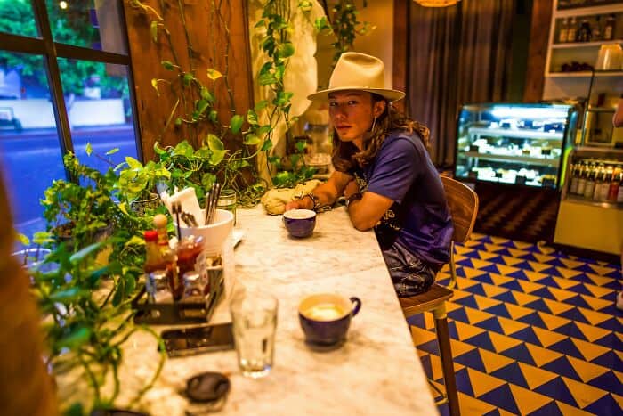 Woman in hat sitting at a cozy café counter with plants and patterned floor.