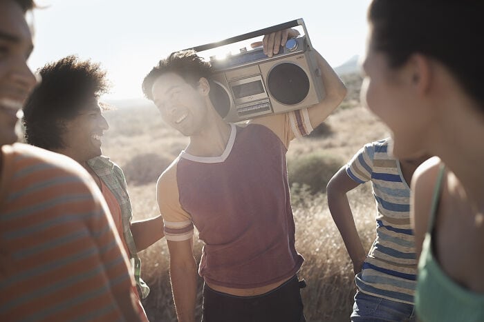 Group of friends enjoying outdoor music with a boombox in a sunny field.