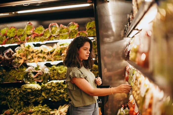 Woman shopping for fresh vegetables in a grocery store produce section.