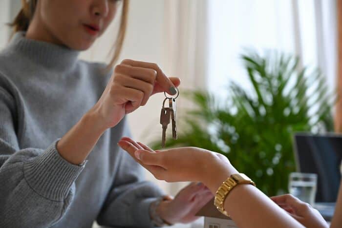 Woman handing over keys to new apartment, close-up of key exchange.