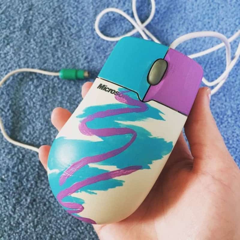 Brightly colored computer mouse with a pink and blue pattern, connected by a white cord on a texture.