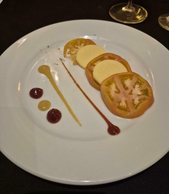 Artistic food presentation with tomato slices and sauces on a white plate.
