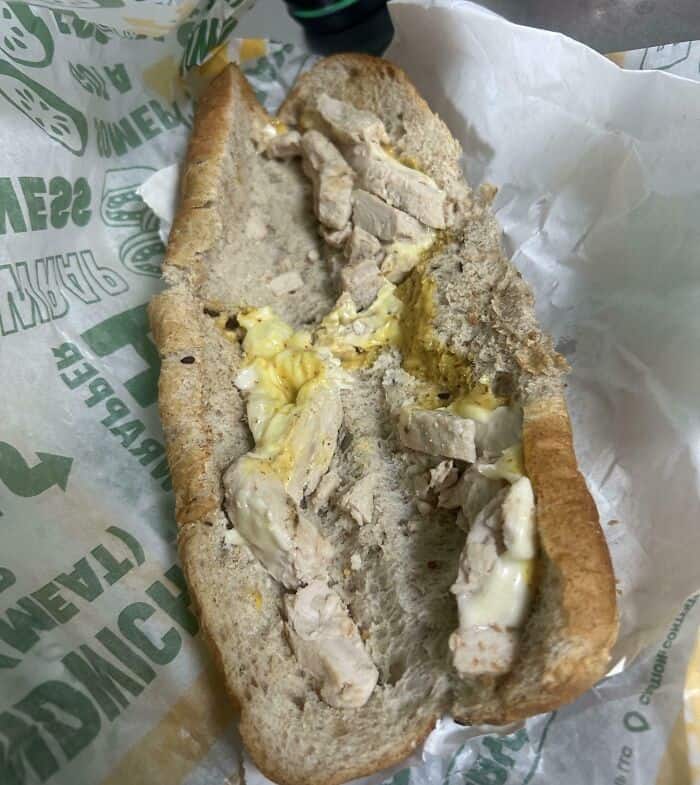 Moldy bread hot dog with spoiled toppings, unappetizing food item.