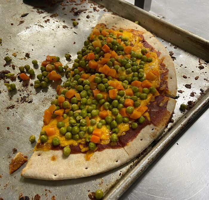 Pizza topped with peas and carrots, looking unappetizing and poorly prepared.