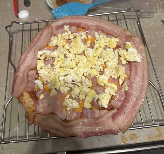 Unusual bacon and scrambled eggs pizza on a wire rack.