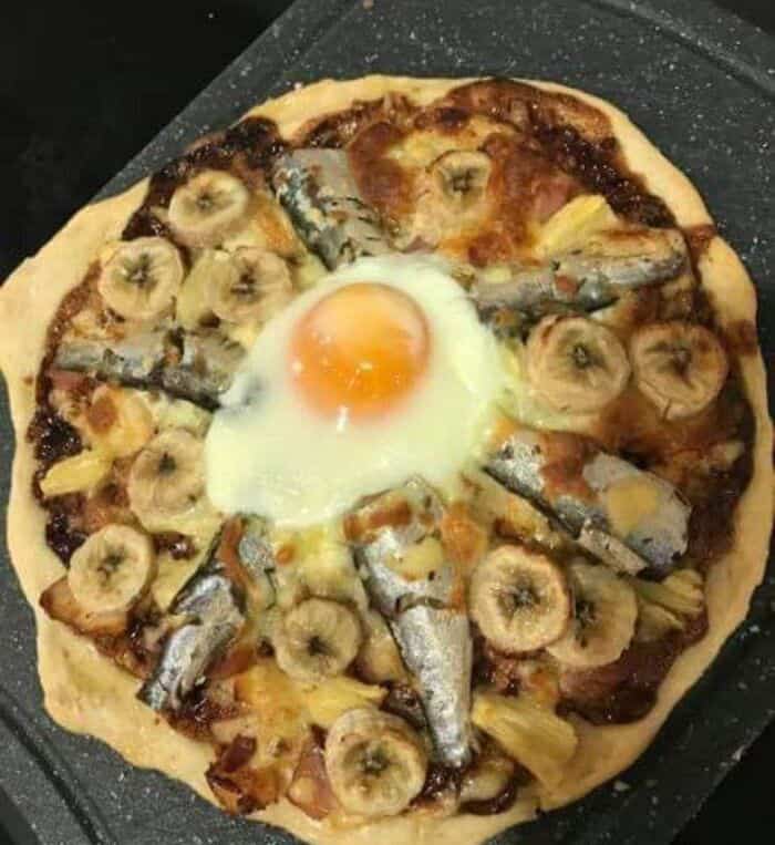 Delicious and unusual pizza topped with bananas, sardines, pineapple, and a fried egg.