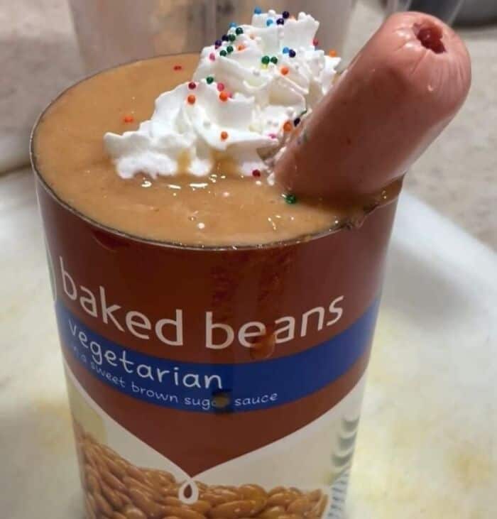 Baked beans with a hot dog in a cup, topped with whipped cream and sprinkles.