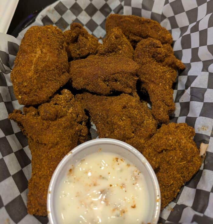 Crispy fried chicken pieces with creamy dipping sauce on checkered paper.