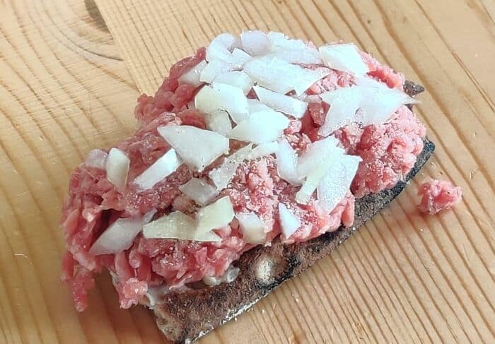 Raw ground meat with chopped onions on a wooden cutting board, highlighting a "cursed food" theme.