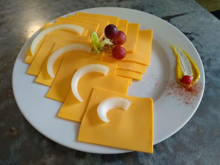 Slices of cheese with grapes and garnishes on a white plate.