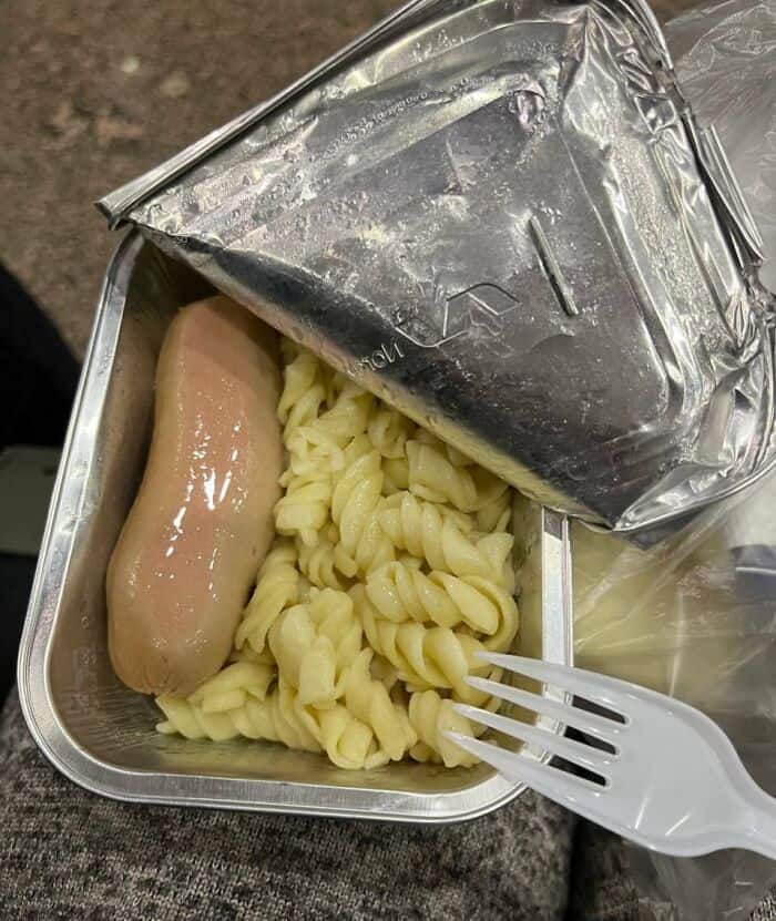 Uncooked hot dog and pasta in a foil container, with a fork, labeled as cursed food.