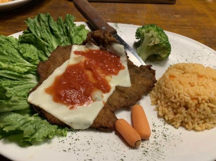 Unappetizing food plate with rice, broccoli, carrots, and a breaded meat cutlet with cheese and sauc.