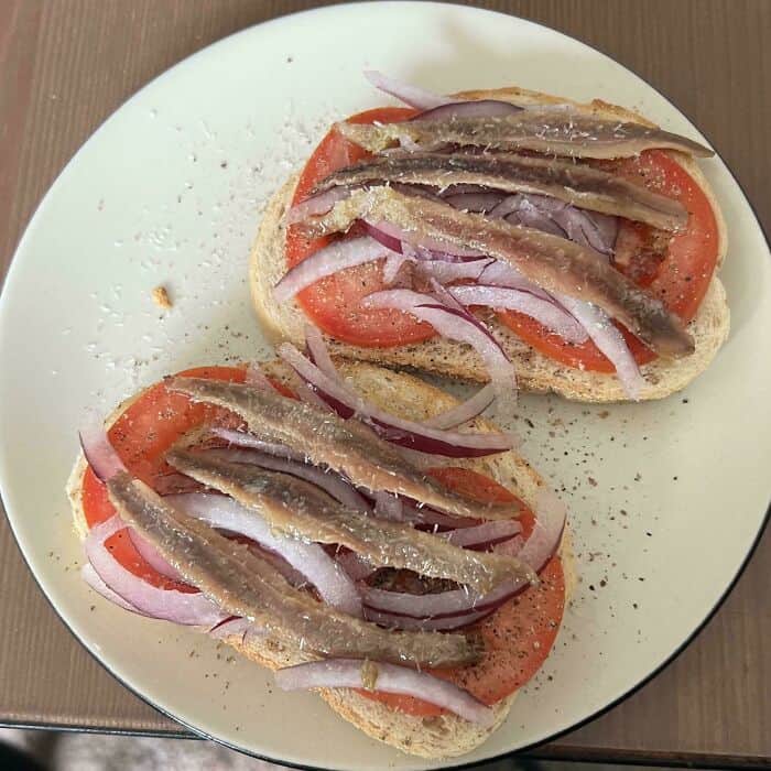 Anchovy-topped tomato and onion open-faced sandwich on bread.